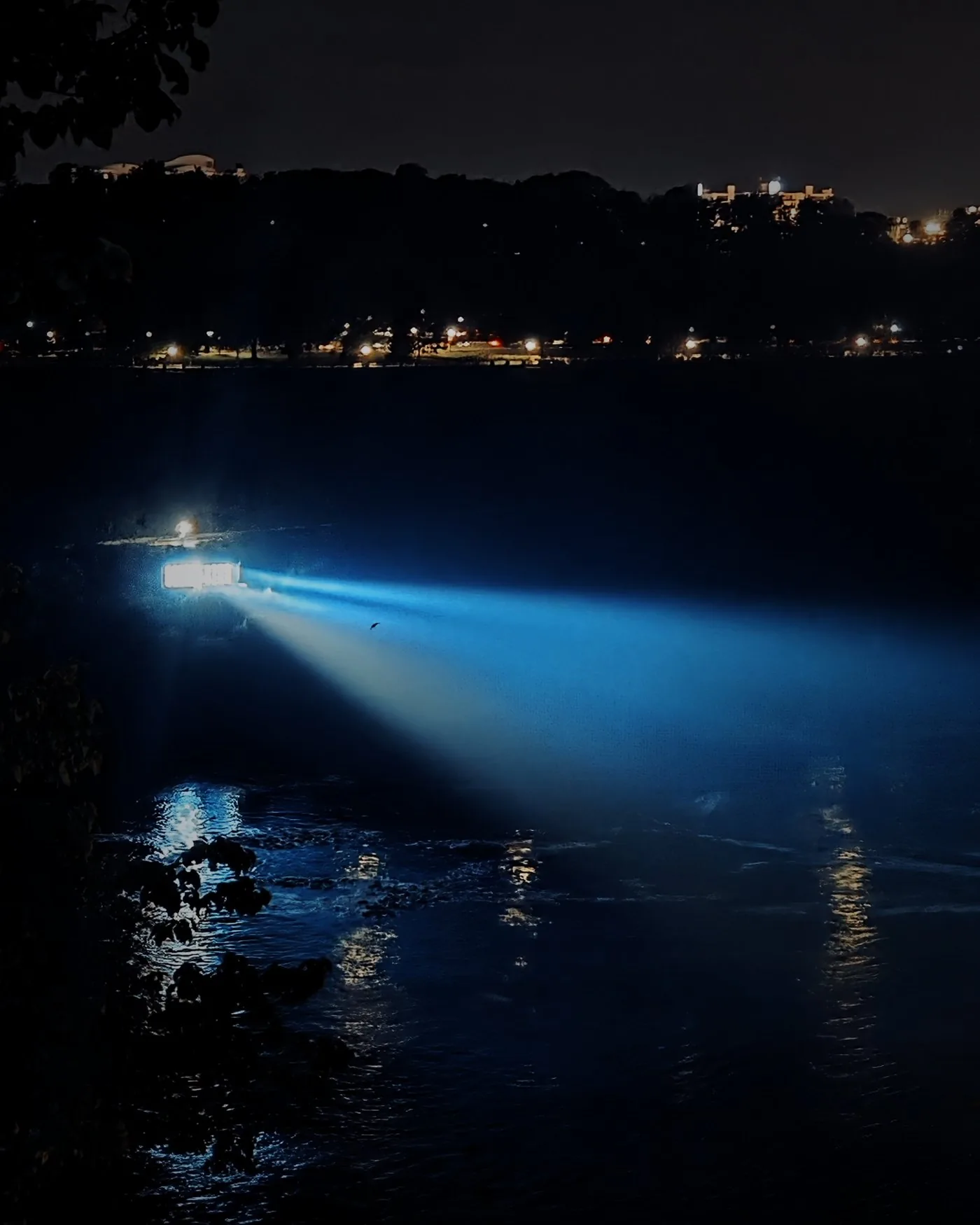 A beam of light crossing dark water at night.